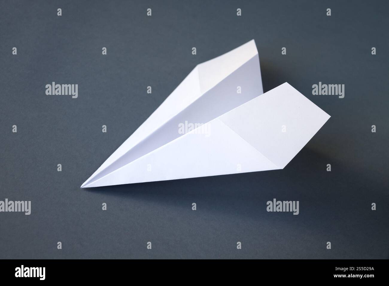 Weißes Papierflugzeug Origami isoliert auf einem leeren grauen Hintergrund. Weißes Papierflugzeug Origami isoliert auf grauem Hintergrund Stockfoto
