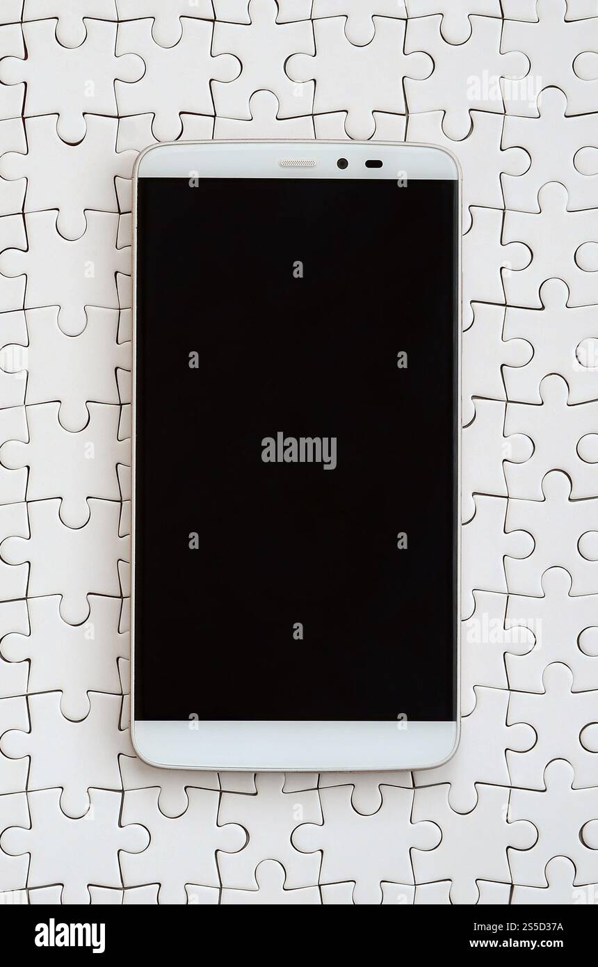 Eine moderne grosse Smartphone mit Touchscreen liegt auf einem weißen Puzzle im zusammengebauten Zustand Stockfoto