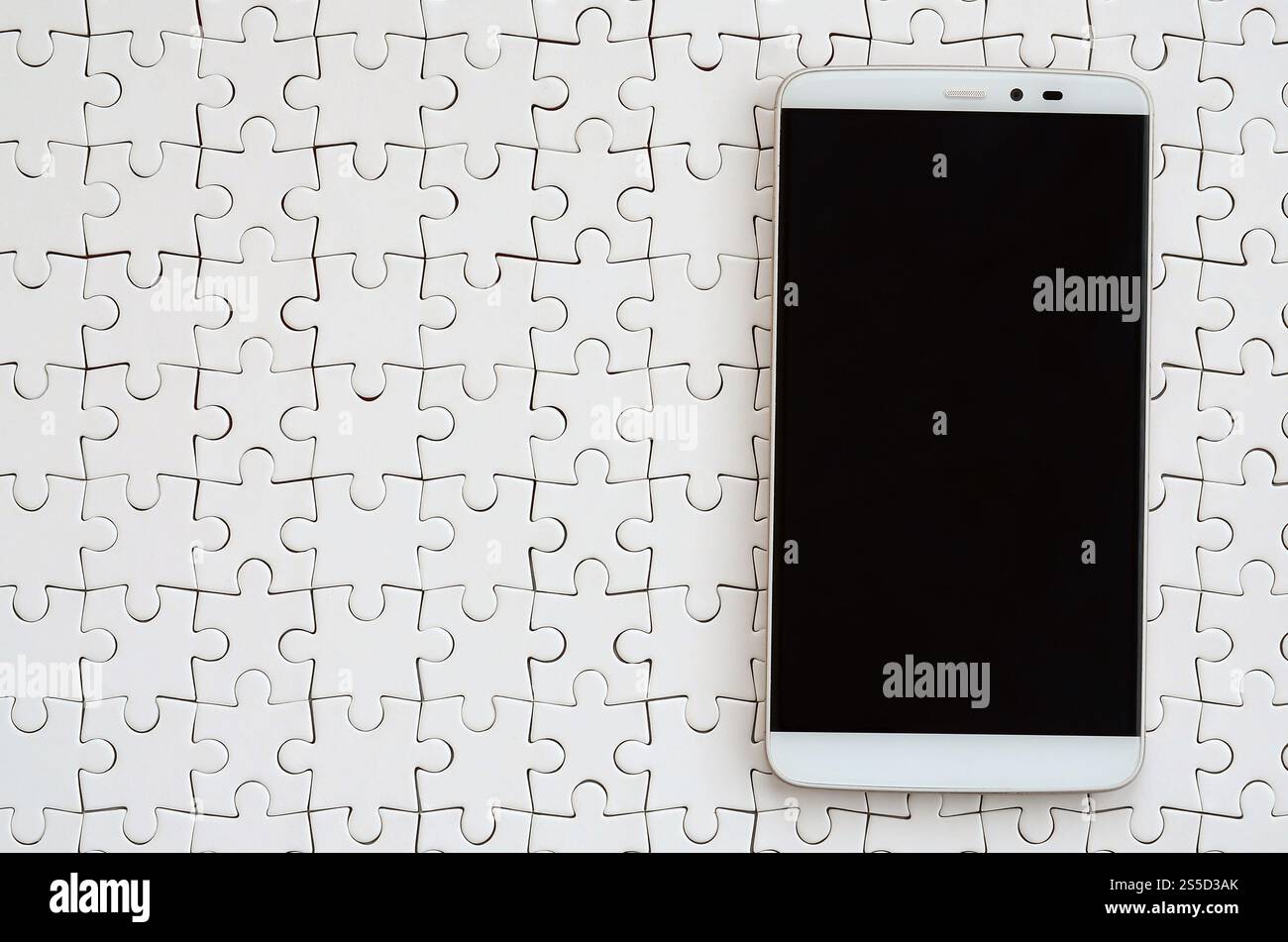 Eine moderne grosse Smartphone mit Touchscreen liegt auf einem weißen Puzzle im zusammengebauten Zustand Stockfoto