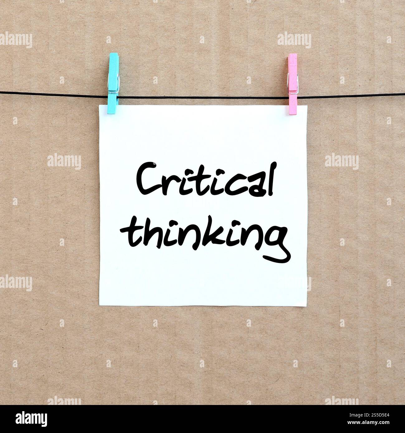 Kritisches Denken. Die Notiz ist auf einem weißen Aufkleber geschrieben, der mit einem Kleiderschrank an einem Seil auf einem Hintergrund aus braunem Karton hängt Stockfoto