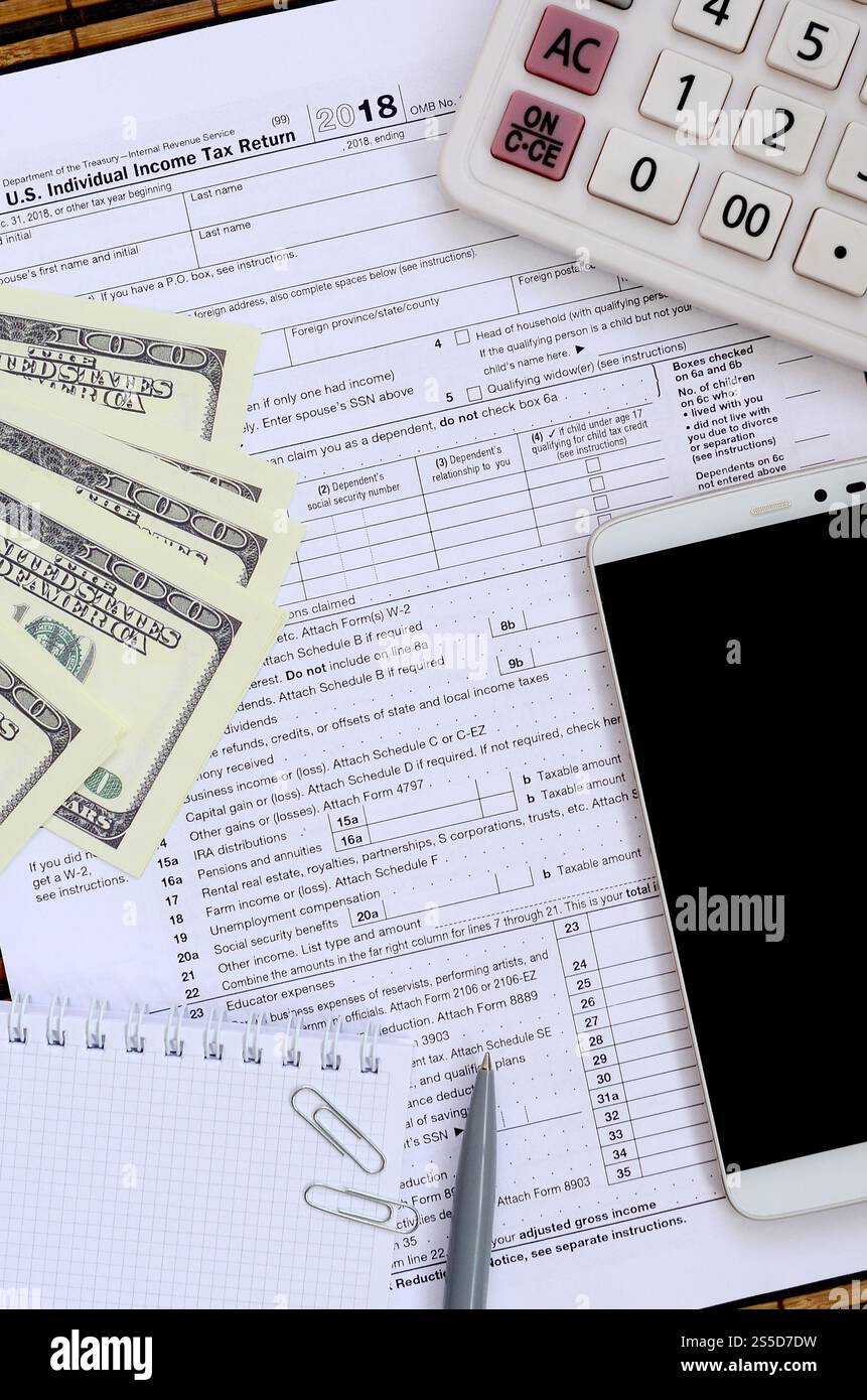 Zusammensetzung der Gegenstände, die auf dem Steuerformular 1040 liegen. Dollarscheine, Stift, Rechner, Smartphone, Büroklammer und Notizblock. Die Zeit, Steuern zu zahlen Stockfoto