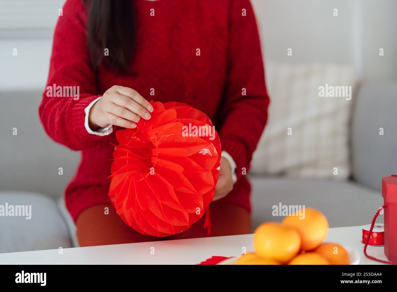 Asiatische Frau, die rote chinesische Neujahrslaterne hält, während sie flach dekoriert ist und traditionelle Anhänger zu den chinesischen Neujahrsfeiern für viel Glück setzt. Stockfoto