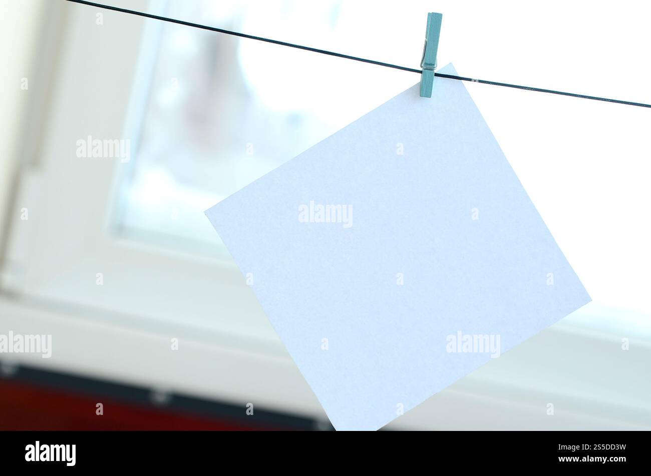 Weiße unbeschriftete Karte am Seil, Fensterglashintergrund. Kreative Erinnerung, kleines Blatt Papier auf Holzkaschentücher, Memo-Hintergrund Stockfoto