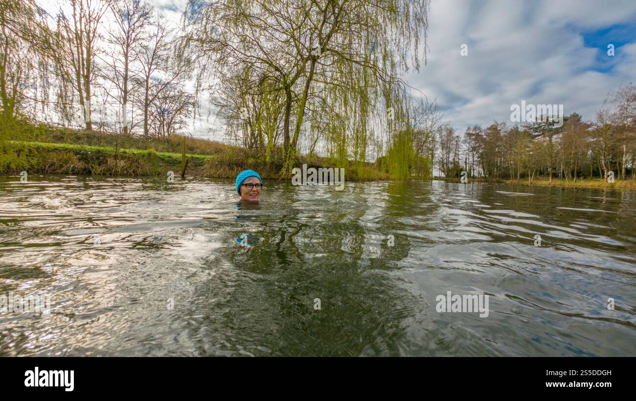 Reife Frau mit Brille und türkisfarbenem Strickmütze Wild Swimming an einem Wintermorgen, UK Stockfoto
