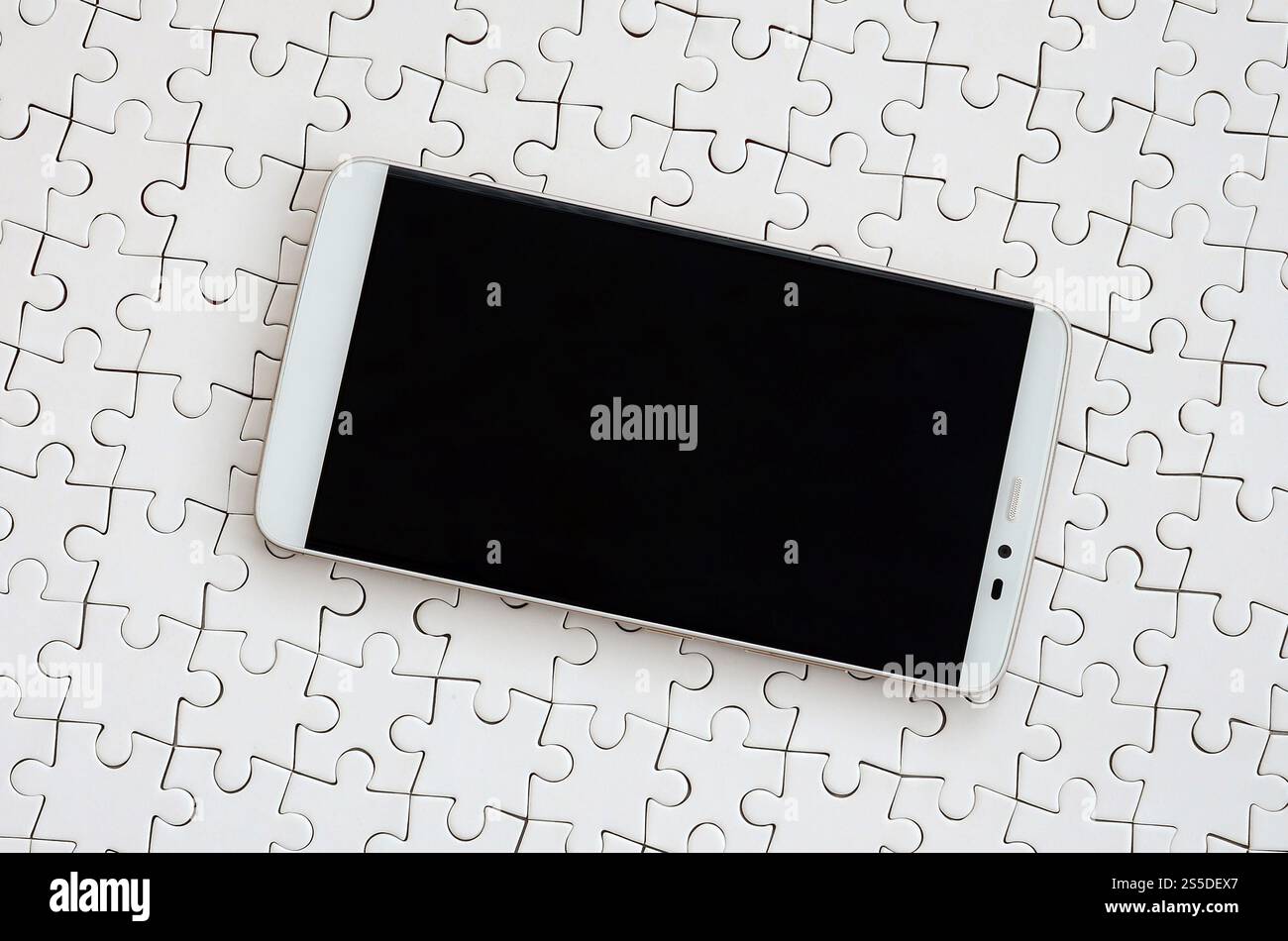 Eine moderne grosse Smartphone mit Touchscreen liegt auf einem weißen Puzzle im zusammengebauten Zustand Stockfoto