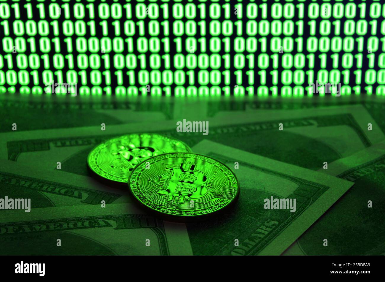 Zwei Bitcoins liegen auf einem Stapel von Dollarscheinen auf dem Hintergrund eines Monitors, der einen Binärcode aus hellgrünen Nullen und eine Einheit auf einem schwarzen zeigt Stockfoto
