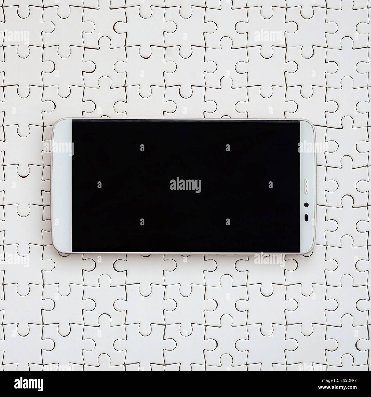 Eine moderne grosse Smartphone mit Touchscreen liegt auf einem weißen Puzzle im zusammengebauten Zustand Stockfoto