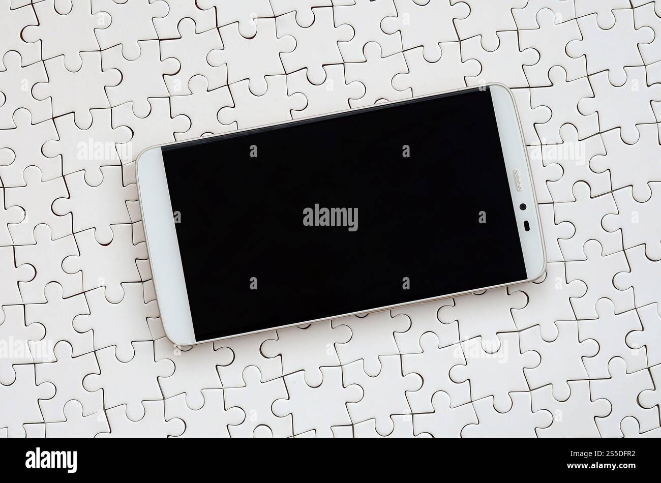 Eine moderne grosse Smartphone mit Touchscreen liegt auf einem weißen Puzzle im zusammengebauten Zustand Stockfoto