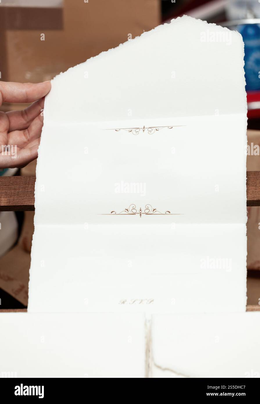 Nahaufnahme eines Handwerkers, der eine gefaltete RSVP-Karte aus handgemachtem Papier präsentiert, die elegantes Design und handwerkliches Können zeigt Stockfoto