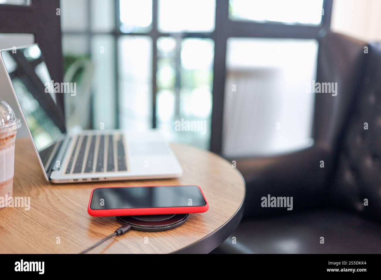 Laden des Mobiltelefonakkus mit dem drahtlosen Gerät in der Tabelle. Smartphone wird auf einem Ladepad aufgeladen. Mobiltelefon in der Nähe des kabellosen Ladegeräts Stockfoto