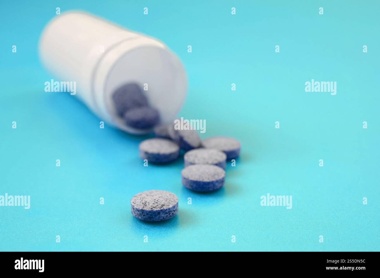 Mehrere graue Tabletten fallen aus der Kunststoffbehälter auf der blauen Fläche. Hintergrundbild über medizinische und pharmazeutische Themen Stockfoto