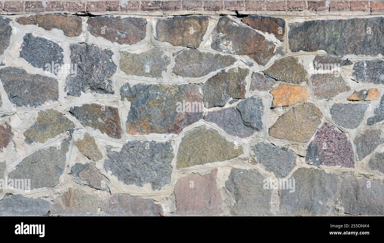 Steinmauerhintergrund - Bauelement. Textur einer dicken und starken Wand aus rauen Steinen verschiedener Formen und Größen. Verwittert und alt befleckt Stockfoto Steinmauerhintergrund - Bauelement. Textur einer dicken und starken Wand aus rauen Steinen verschiedener Formen und Größen. Verwittert und alt befleckt Stockfoto