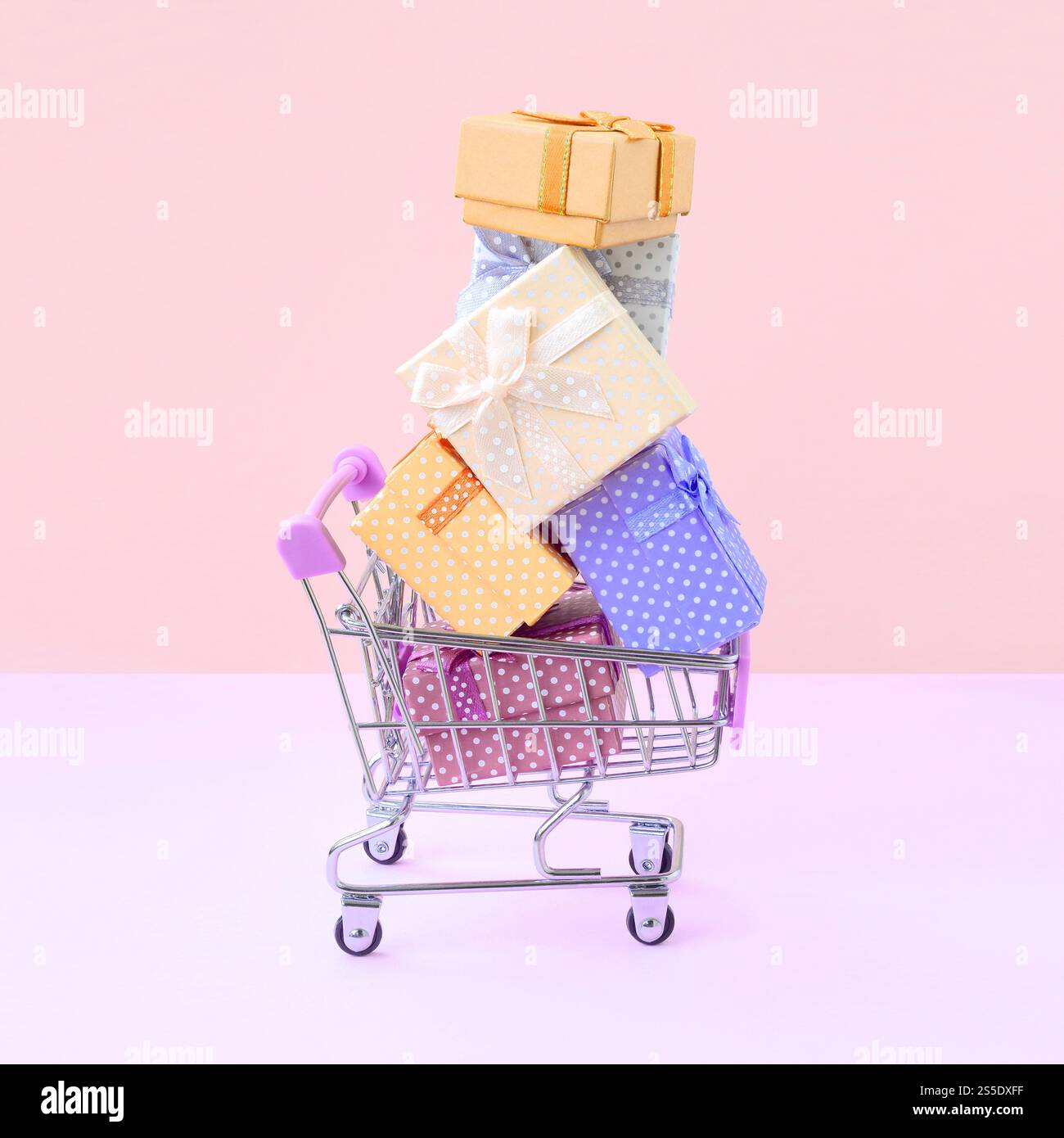 Viele bunte Geschenkboxen im Einkaufswagen des Supermarktes auf pfirsichfarbenem Hintergrund. Geschenke für Winterferien. Geschenkboxen für Winterferien in Stockfoto