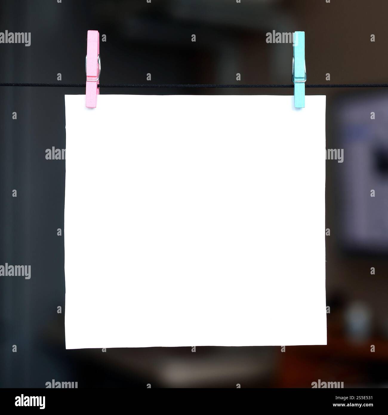 Weiße unbeschriftete Karte am Seil, dunkler Bürohintergrund. Kreative Erinnerung, kleines Blatt Papier auf Holzkaschentücher, Memo-Hintergrund Stockfoto