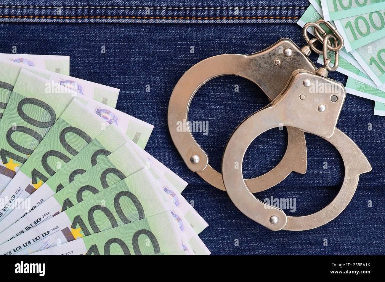 Der Fan von vielen Euro-Scheinen und Polizeihandschellen ist auf einer dunklen Jeansfläche. Hintergrundbild Stockfoto