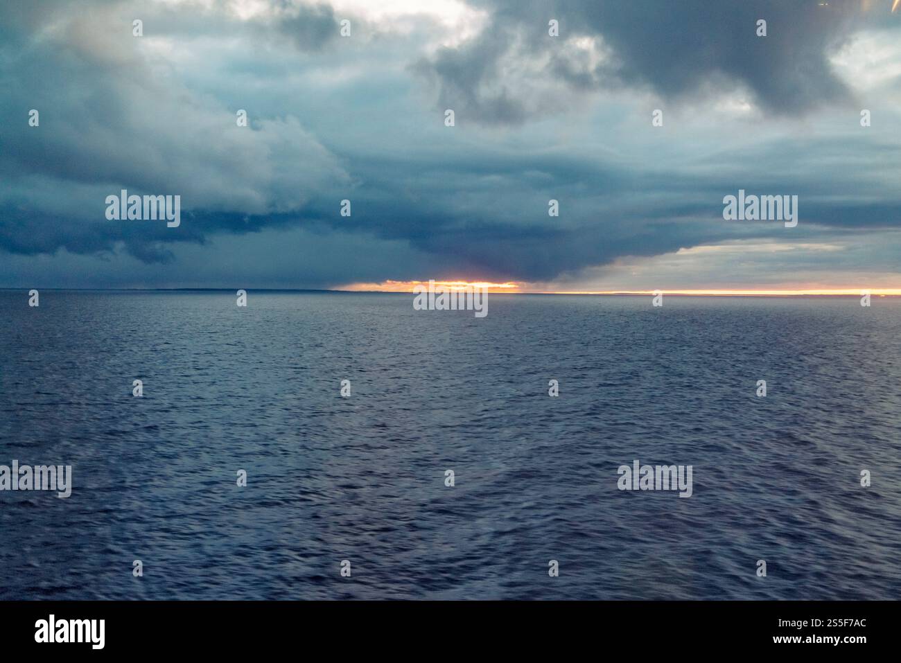Sonnenaufgang auf dem Meer mit dunklen Sturmwolken und einem Sonnenstrahl, der durch den Horizont an der ostsee von Finnland bricht Stockfoto