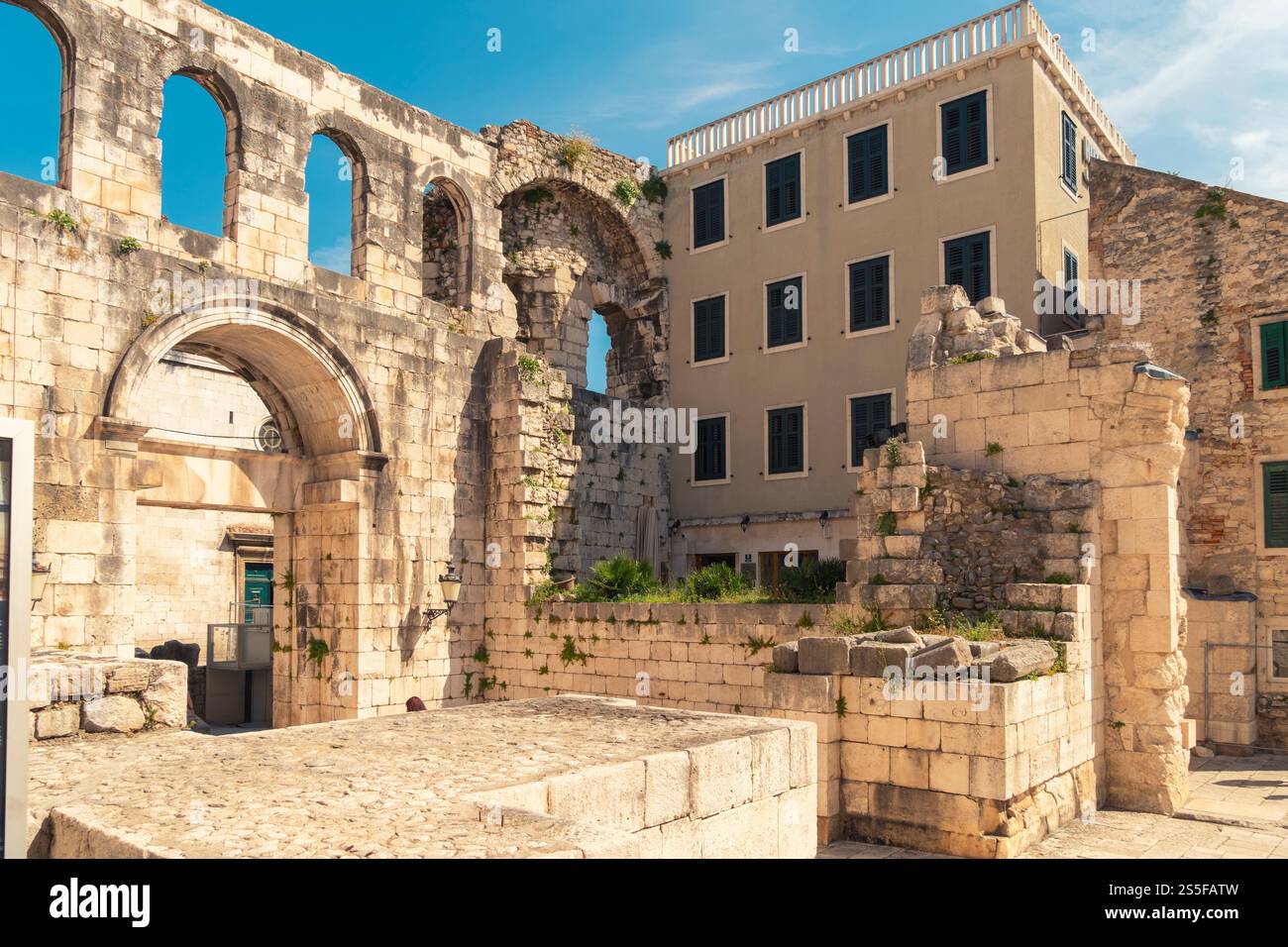 Antike Steinbögen stehen neben einem modernen Gebäude unter einem klaren blauen Himmel, die historische Architektur mit zeitgenössischem Bau der Wiese von Königin Helena, Split, Kroatien, verbinden Stockfoto