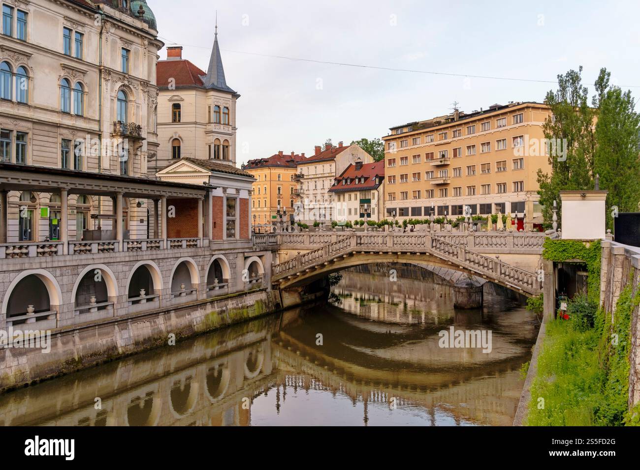 Ein ruhiger Blick auf eine europäische Stadt mit historischen Gebäuden und einer Dreifachbrücke über einen ruhigen Kanal von Ljubljana in der Abenddämmerung, Ljubljana, Slowenien Stockfoto