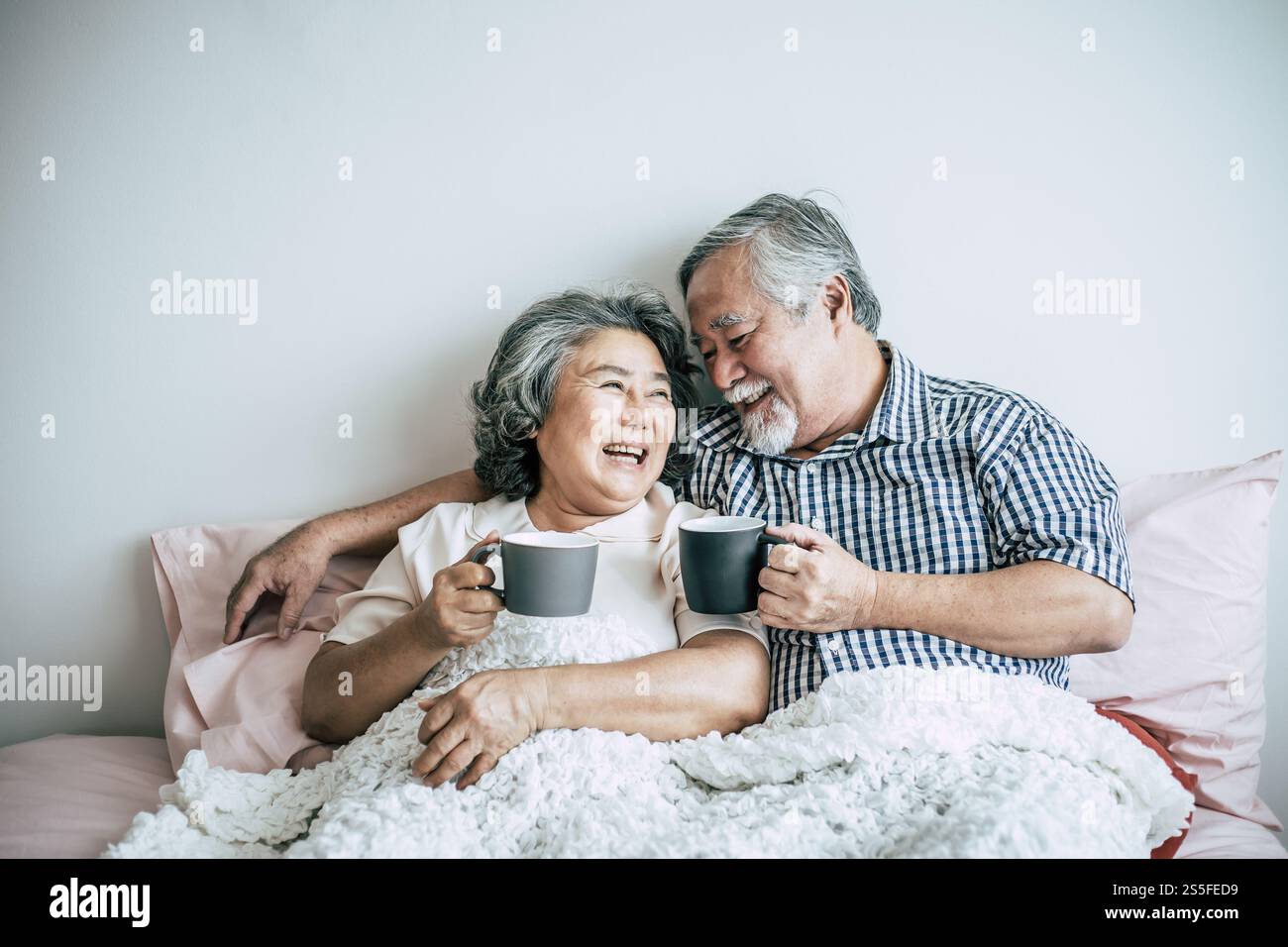 Seniorenpaar lacht beim Kaffeetrinken im Schlafzimmer Stockfoto