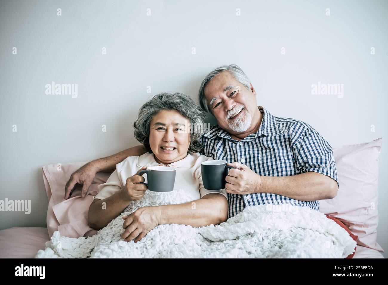 Seniorenpaar lacht beim Kaffeetrinken im Schlafzimmer Stockfoto