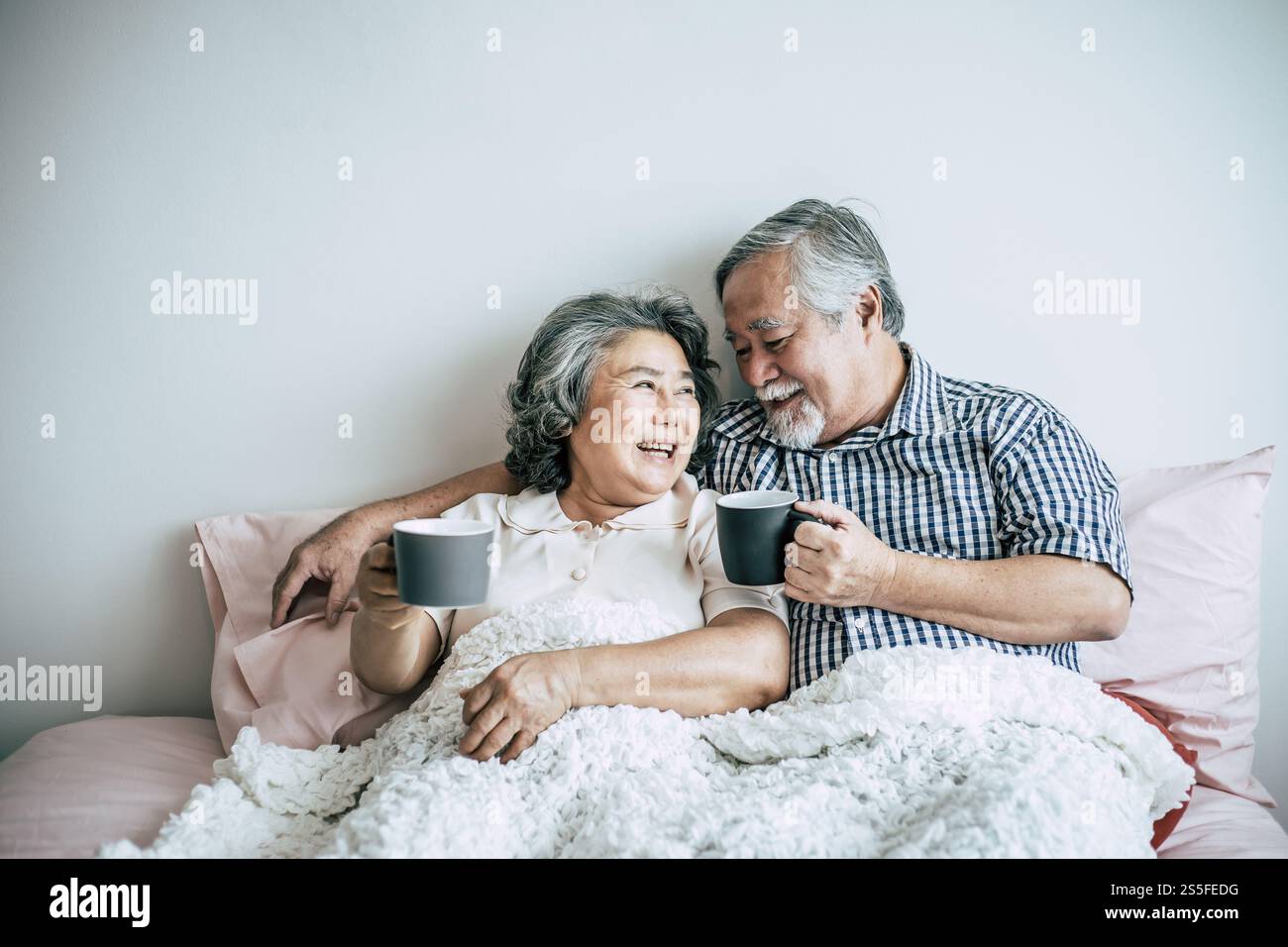 Seniorenpaar lacht beim Kaffeetrinken im Schlafzimmer Stockfoto
