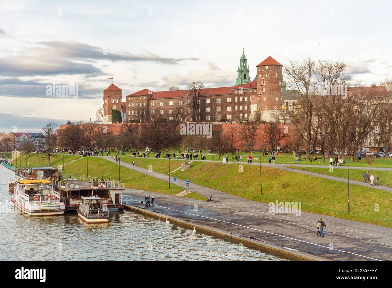 Blick auf den Sonnenuntergang über einem ruhigen Fluss mit Menschen, die entlang des Dammes schlendern, und Krakau Burg auf dem Hügel im Hintergrund, Krakau, Polen Stockfoto