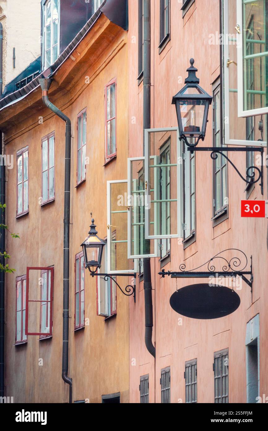 Orange und pinkfarbene Fassaden alter Gebäude mit Vintage-Straßenlaternen und Beschilderung in einer stimmungsvollen Gasse in Gamla Stan, Stockholm, Schweden Stockfoto