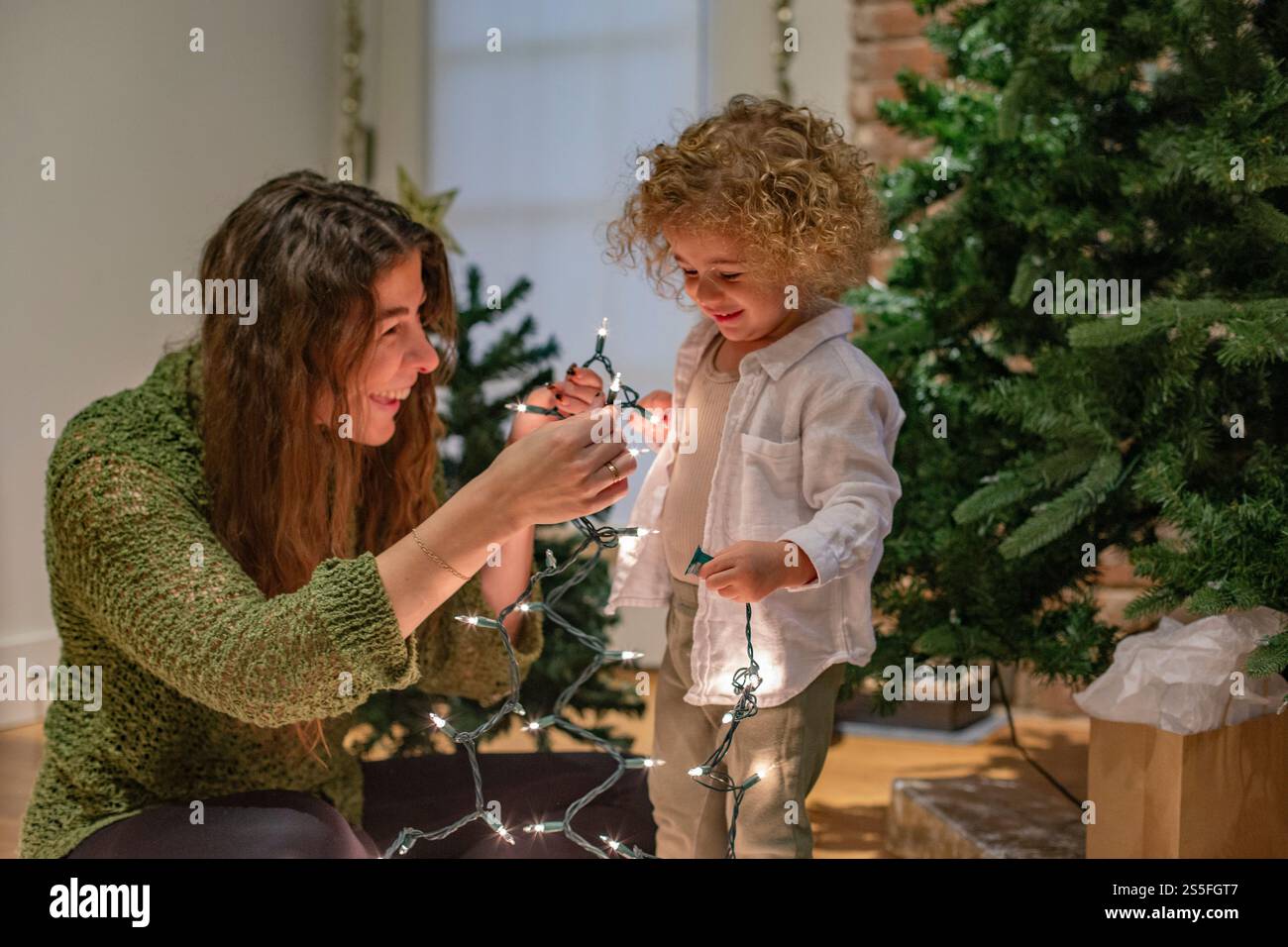 Lächelnde Frau und Kind schmücken einen Weihnachtsbaum mit Lichterketten im Innenbereich, Ohio, USA Stockfoto