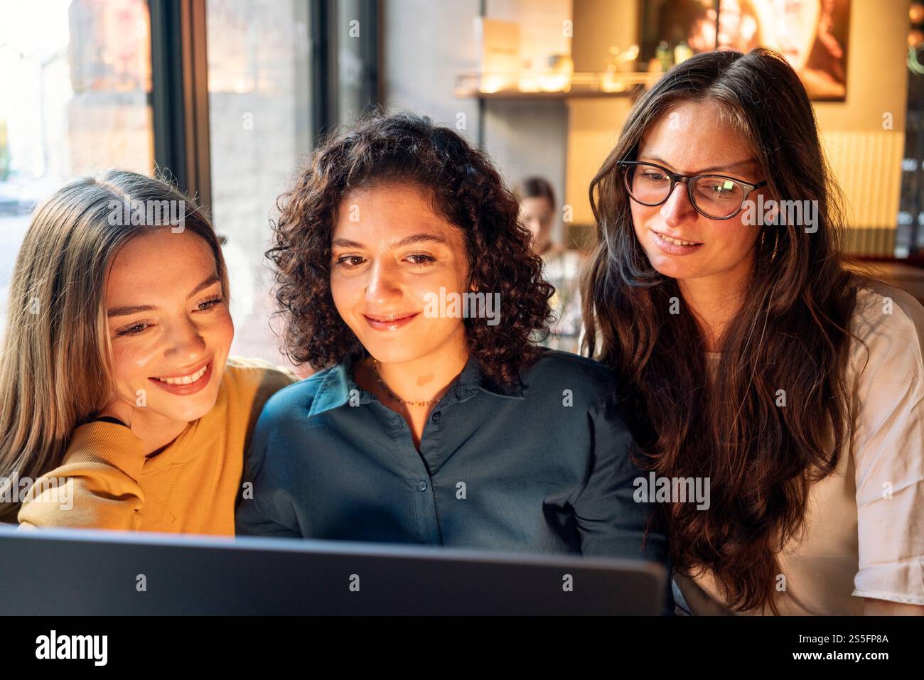 Drei Frauen versammelten sich eng um einen Laptop und überprüften intensiv Inhalte auf dem Bildschirm mit einer warmen Innenbeleuchtung, Berlin, Deutschland Stockfoto