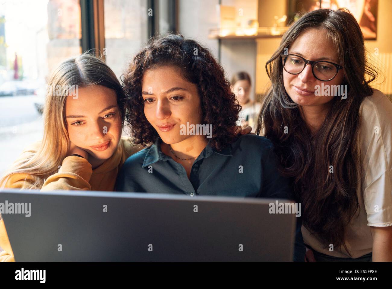 Drei Frauen versammelten sich eng um einen Laptop und überprüften intensiv Inhalte auf dem Bildschirm mit einer warmen Innenbeleuchtung, Berlin, Deutschland Stockfoto