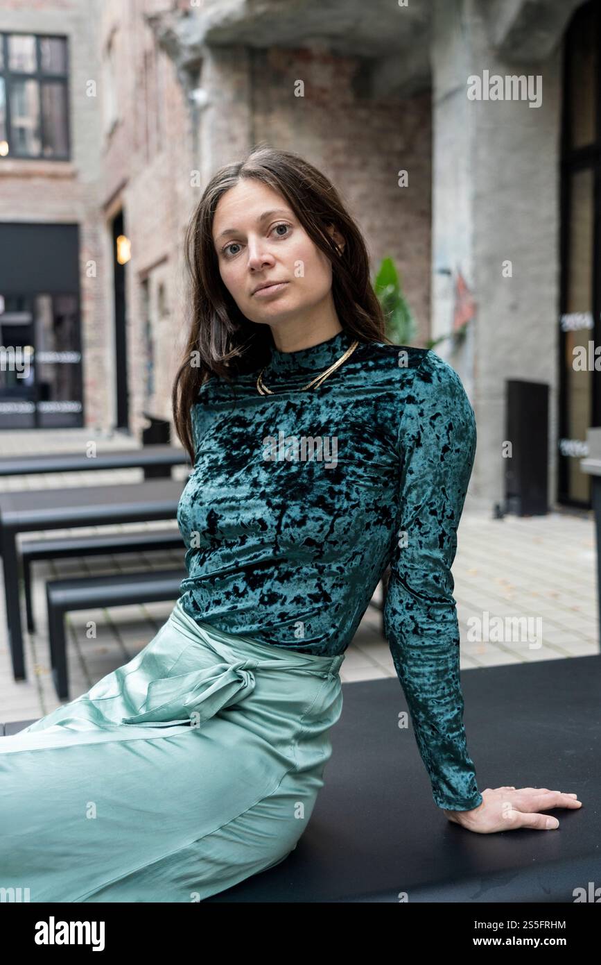 Junge Frau in Samttop und grünem Rock, die draußen auf einer Bank sitzt, Berlin, Deutschland Stockfoto