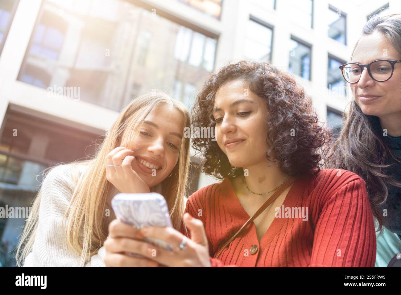Drei Frauen teilen einen freudigen Moment, um gemeinsam Inhalte auf einem Smartphone im Freien anzusehen, Berlin, Deutschland Stockfoto