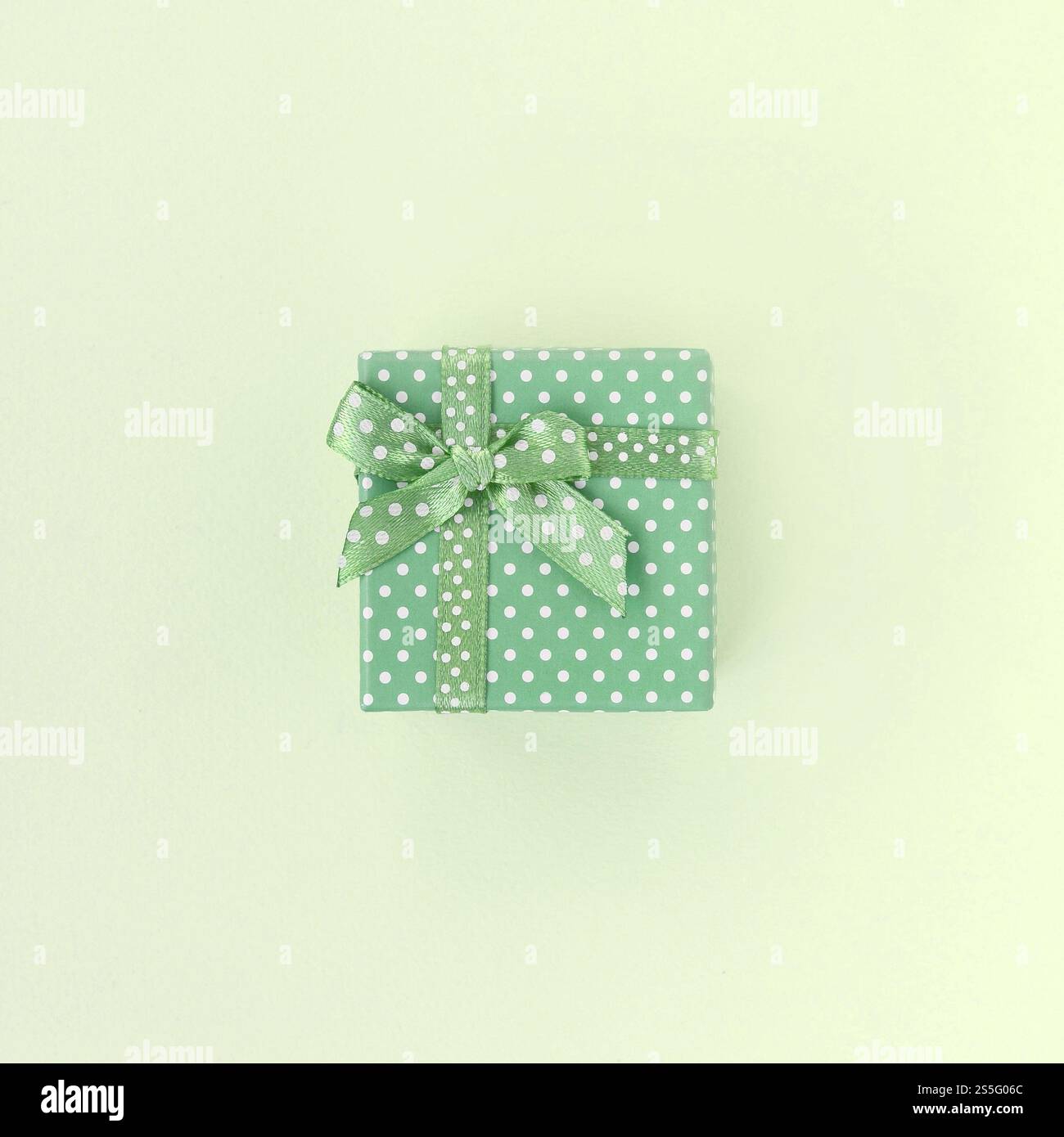 Kleine grüne Geschenkbox mit Band liegt auf kalkfarbenem Hintergrund. Minimalistischer, flacher Blick von oben. Kleine grüne Geschenkbox mit Band liegt auf kalkfarbenem Hintergrund Stockfoto