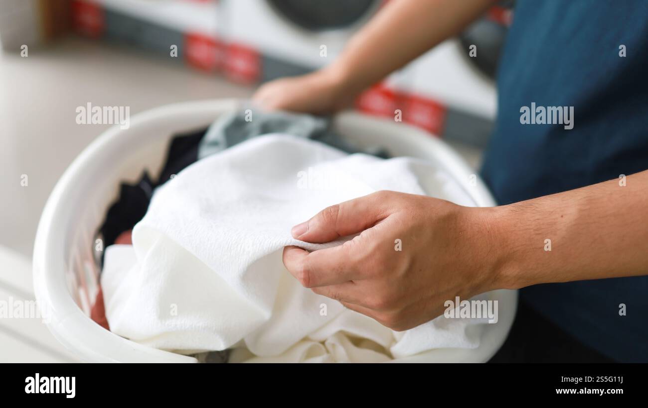 Hausmann mit Korb und schmutziger Wäsche gewaschene Kleidung im Waschraum. Waschmaschine im Wäschereigeschäft Konzept Stockfoto