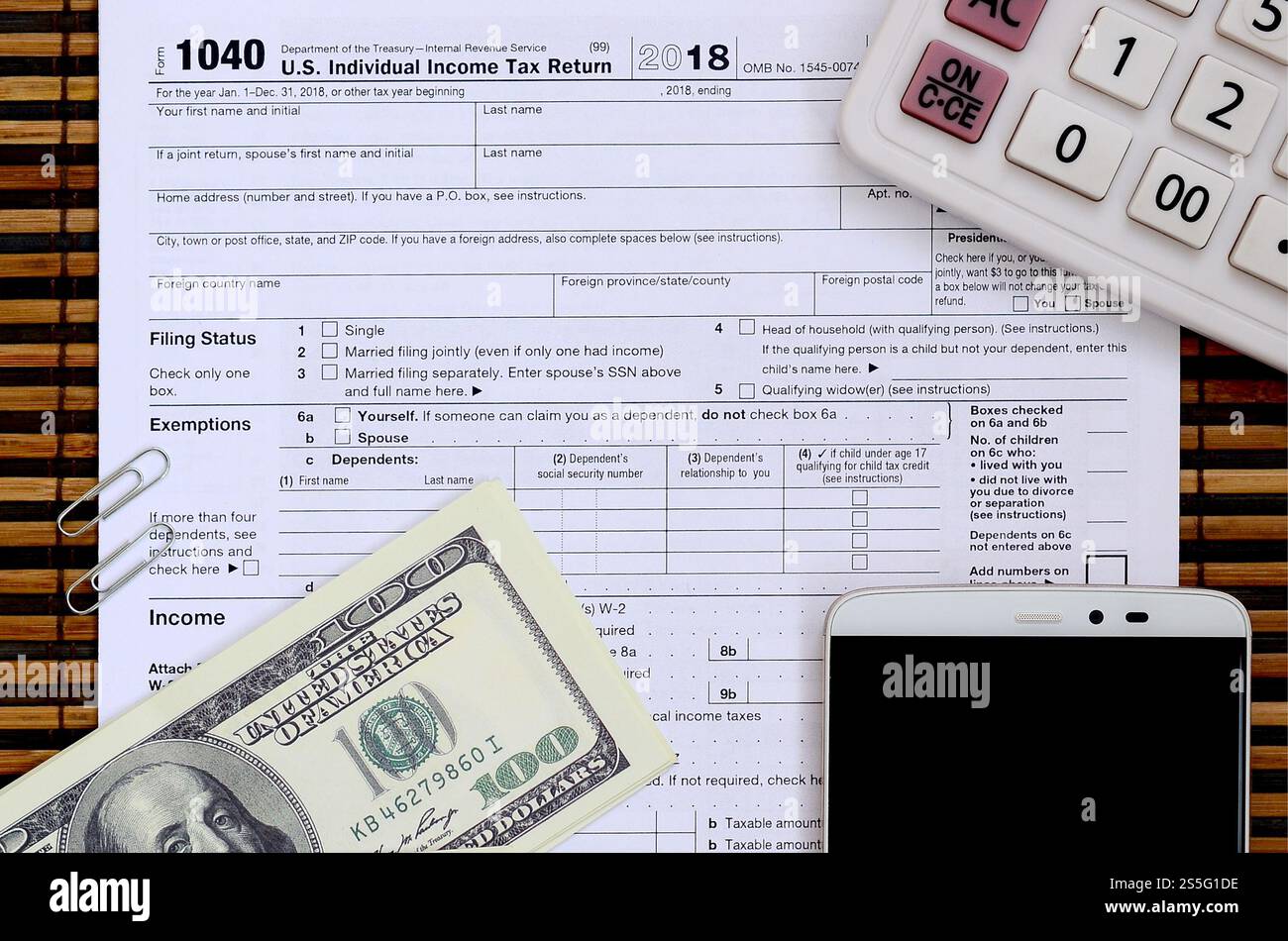 Zusammensetzung der Gegenstände, die auf dem Steuerformular 1040 liegen. Dollarscheine, Taschenrechner, Smartphone, Büroklammer und Notizblock. Die Zeit, Steuern zu zahlen Stockfoto