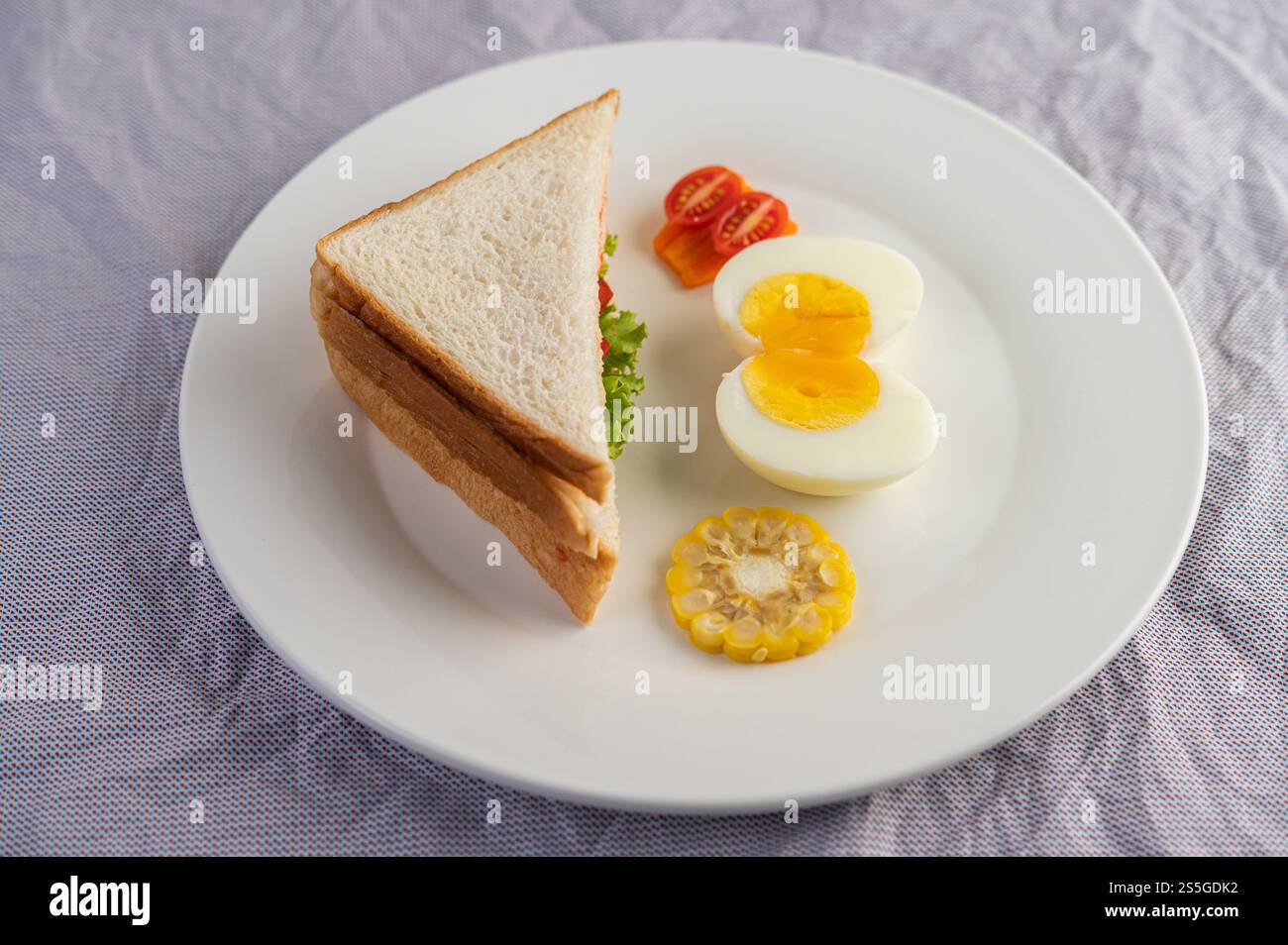 Amerikanisches Frühstück auf weißem Hintergrund mit gekochten Eiern, Mais, Tomaten und Sandwich auf weißem Teller. Stockfoto