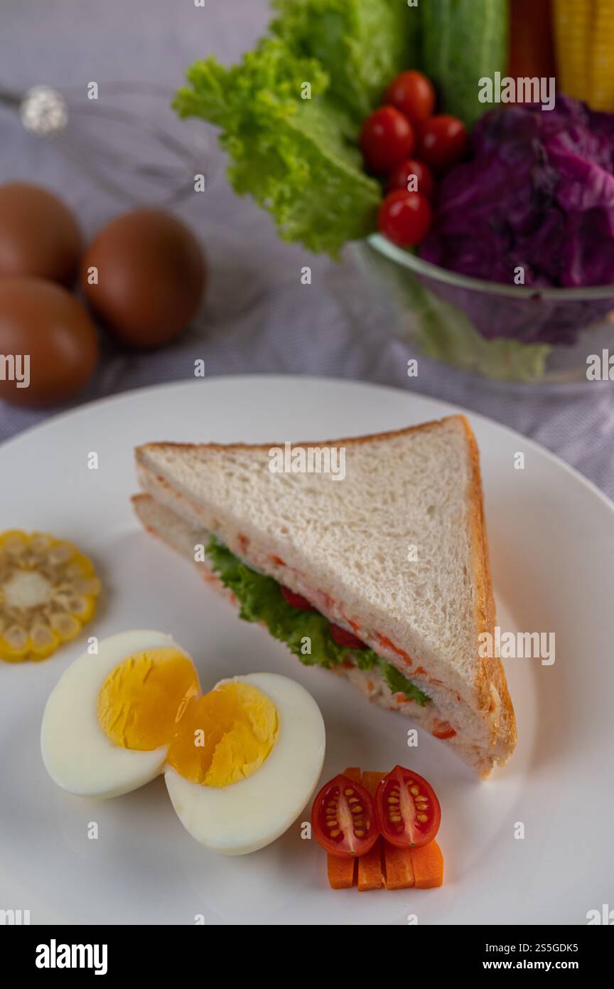 Amerikanisches Frühstück auf weißem Hintergrund mit gekochten Eiern, Mais, Tomaten und Sandwich auf weißem Teller. Stockfoto