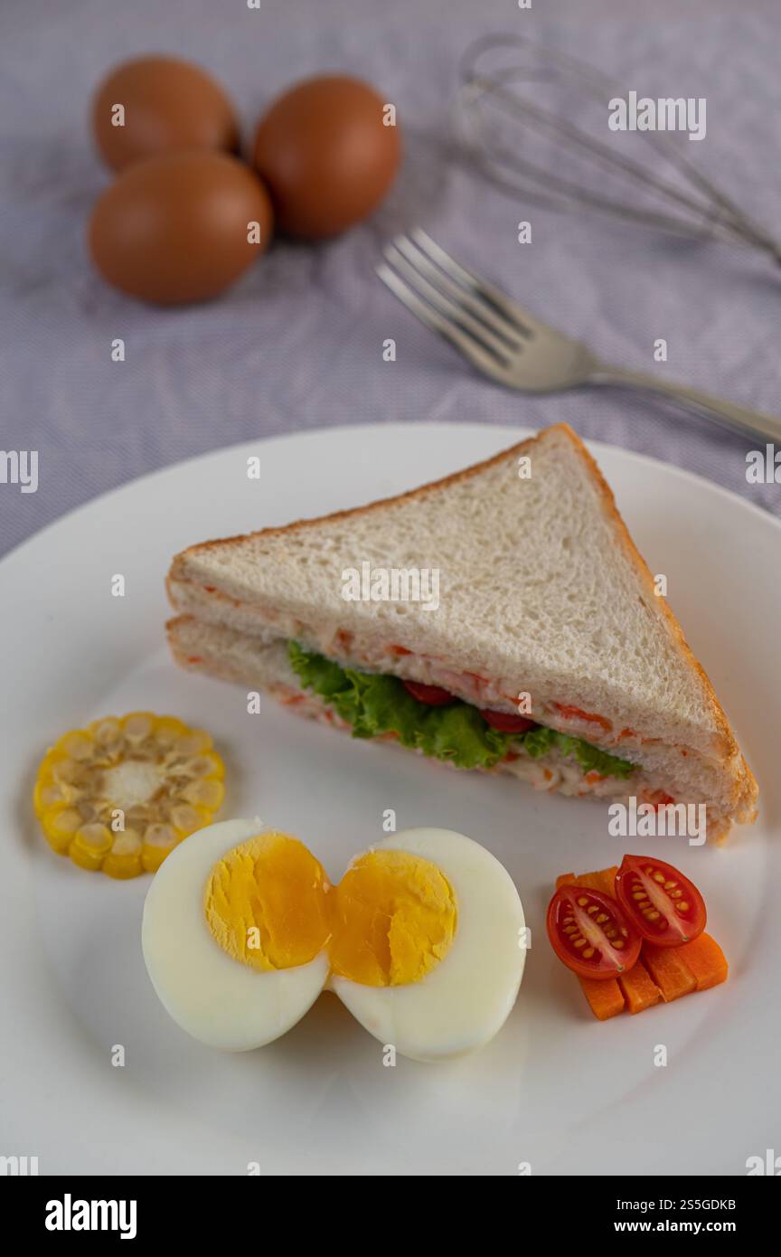 Amerikanisches Frühstück auf weißem Hintergrund mit gekochten Eiern, Mais, Tomaten und Sandwich auf weißem Teller. Stockfoto