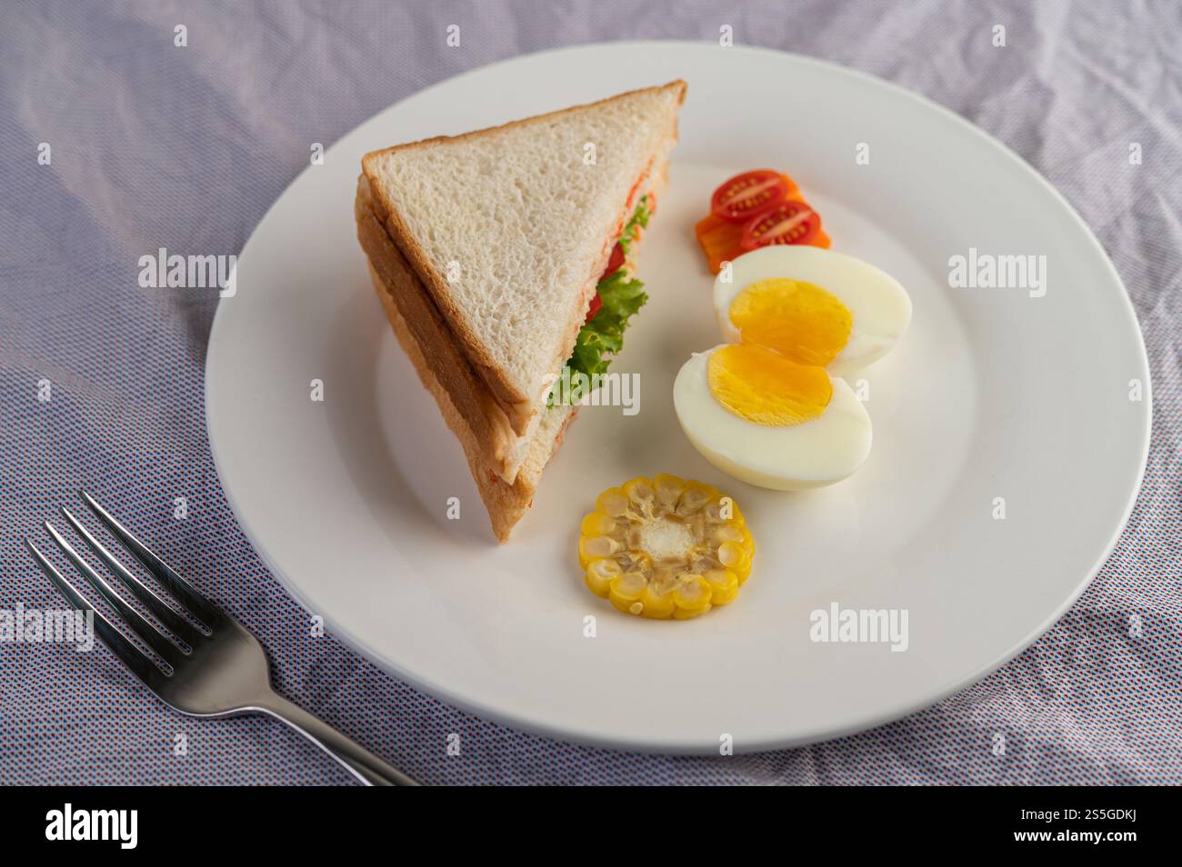 Amerikanisches Frühstück auf weißem Hintergrund mit gekochten Eiern, Mais, Tomaten und Sandwich auf weißem Teller. Stockfoto
