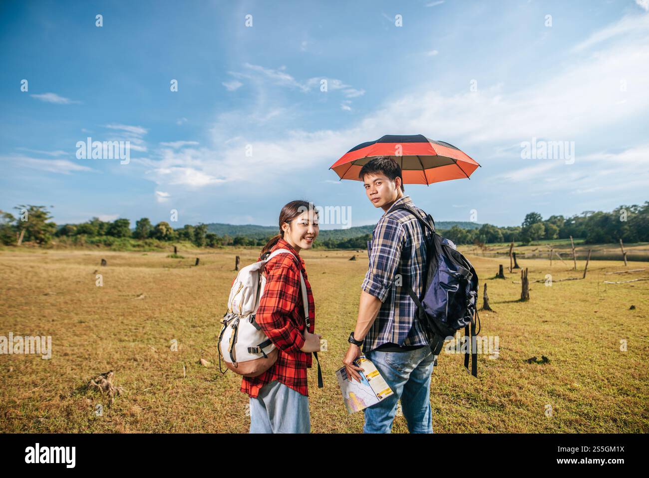 Sowohl männliche als auch weibliche Touristen tragen einen Rucksack, der auf dem Rasen steht und Männer Regenschirme verteilen. Stockfoto