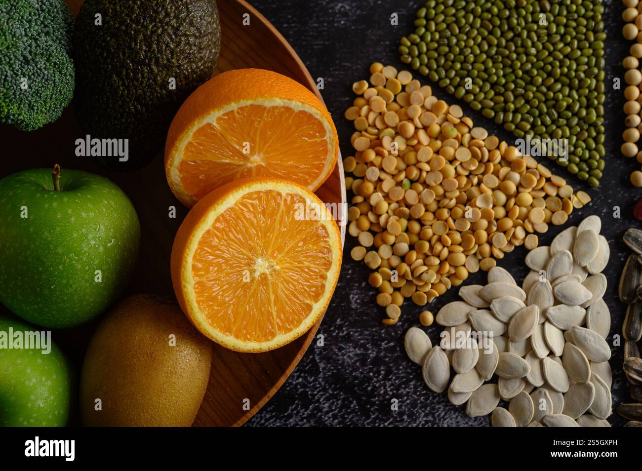 Leguminosen mit Orange in zwei Hälften, kivi und Apfel auf schwarzem Zementboden. Stockfoto