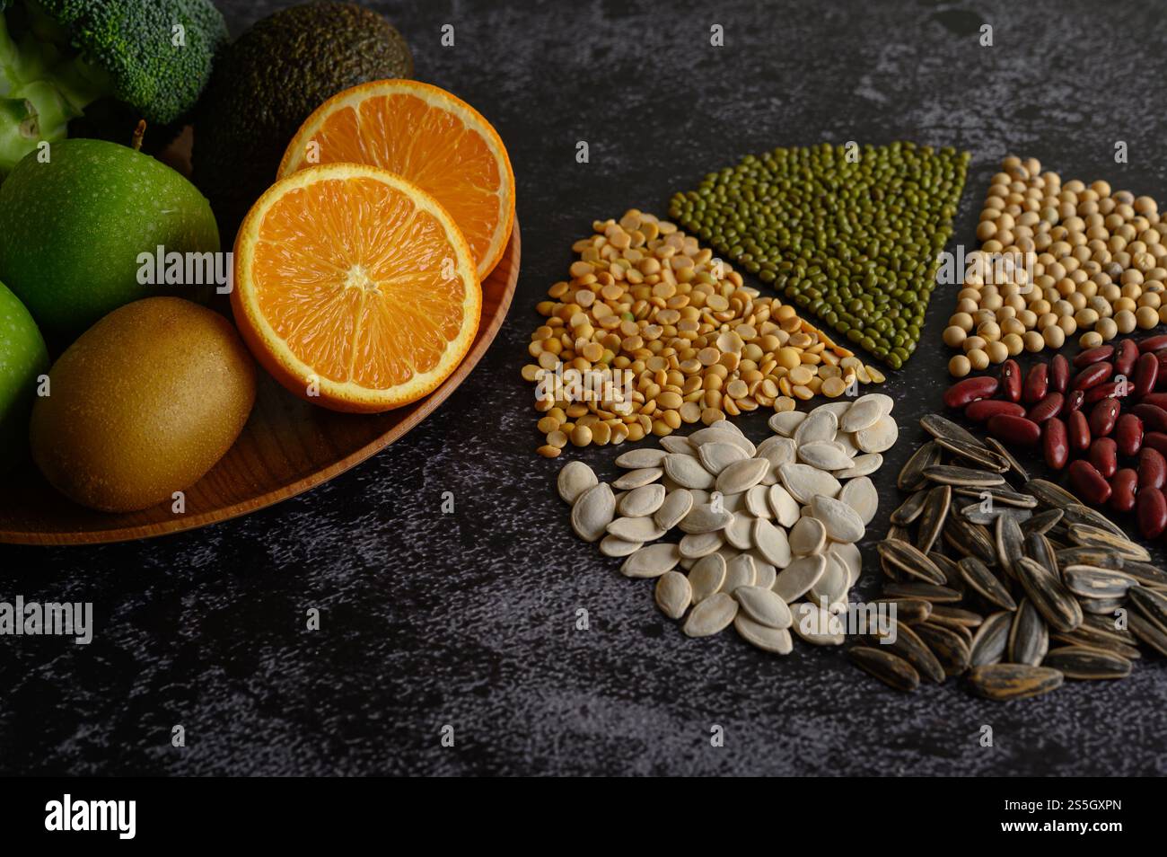 Leguminosen mit Orange in zwei Hälften, kivi und Apfel auf schwarzem Zementboden. Stockfoto