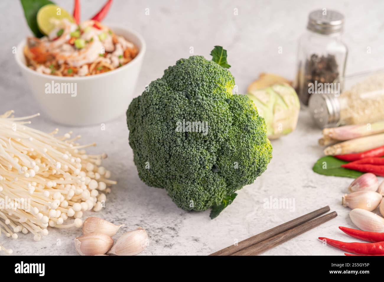 Brokkoli, goldener Nadelpilz, Essstäbchen, Knoblauch und Chilis auf weißem Zementboden. Stockfoto