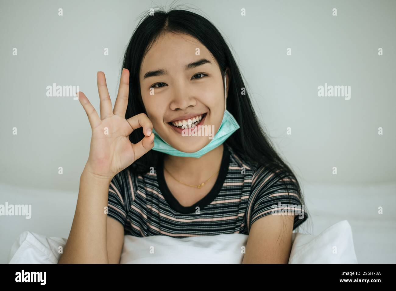 Mädchen mit Hygienemaske, gestreiftem Hemd und Handsymbol, okay Stockfoto