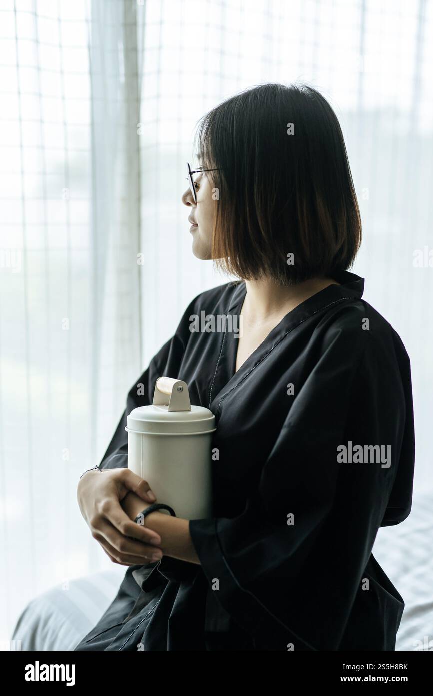 Die Frau trägt ein schwarzes Gewand und umarmt Tiffin und schaut nach draußen. Stockfoto