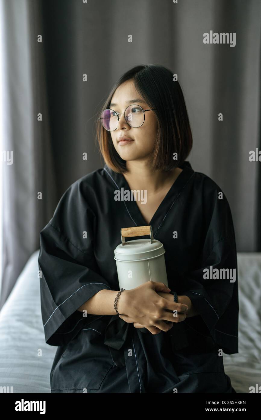 Die Frau trägt ein schwarzes Gewand und umarmt Tiffin und schaut nach draußen. Stockfoto