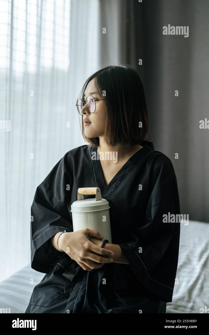 Die Frau trägt ein schwarzes Gewand und umarmt Tiffin und schaut nach draußen. Stockfoto