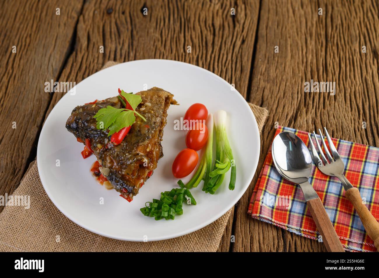 Frittierte Fischköpfe mit Chili auf einem weißen Teller mit Tomaten und Frühlingszwiebeln. Stockfoto