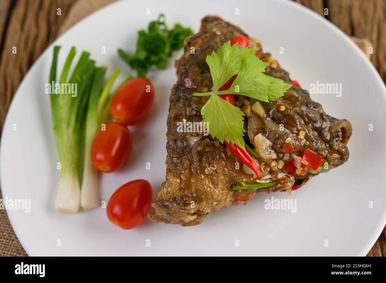 Frittierte Fischköpfe mit Chili auf einem weißen Teller mit Tomaten und Frühlingszwiebeln. Stockfoto