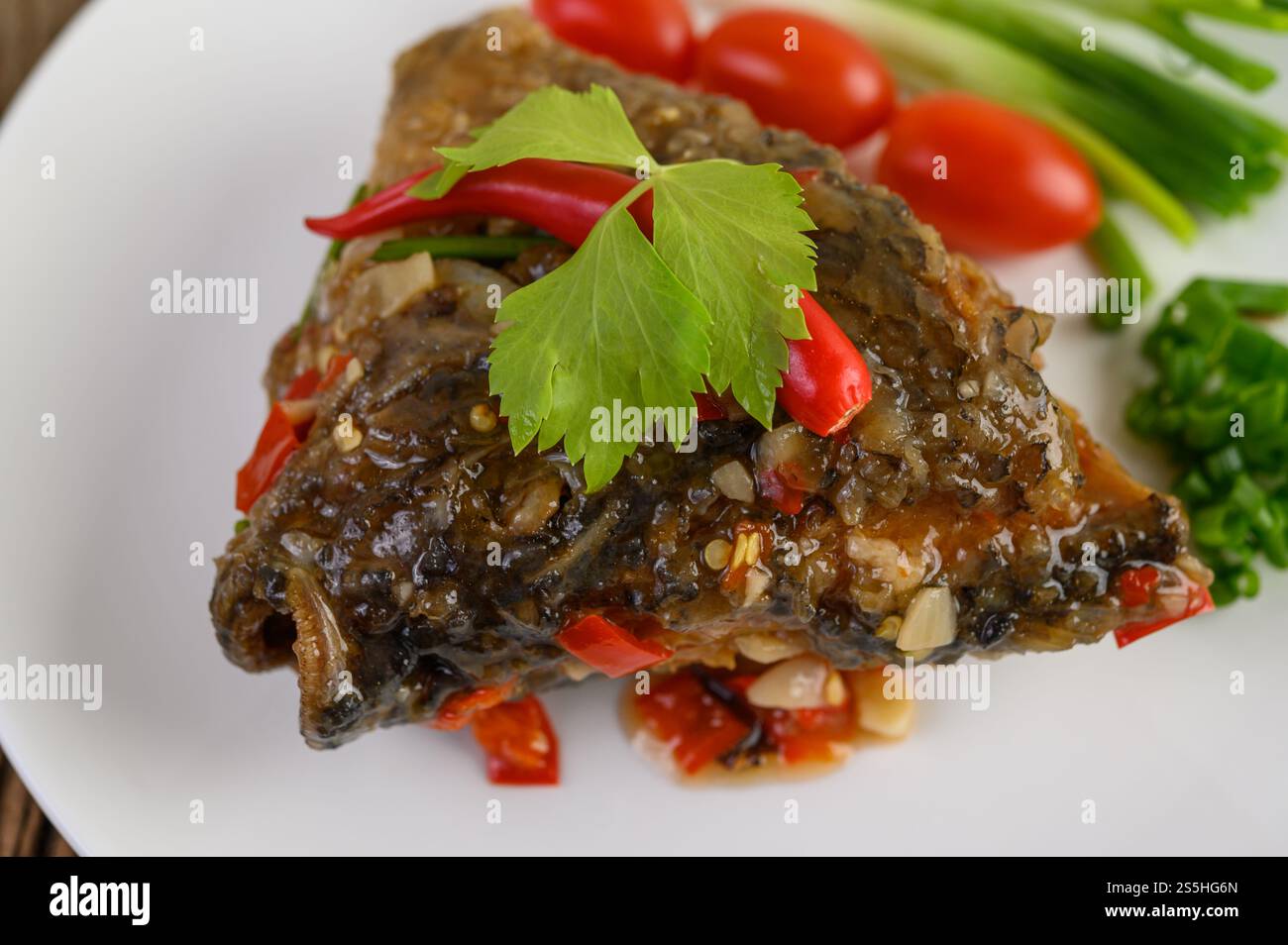 Frittierte Fischköpfe mit Chili auf einem weißen Teller mit Tomaten und Frühlingszwiebeln. Stockfoto